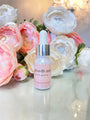 Pink glass bottle of BeautyNomix Growth Assist lash and brow growth oil with dropper, surrounded by white and pink flowers.
